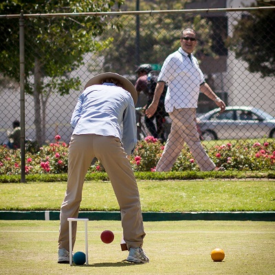 Barbara Doerr executes a reverse jump shot as Dr. Kamal walks past the Pasadena Croquet Club court in Central Park, Pasadena. | Photo by Eric Harris